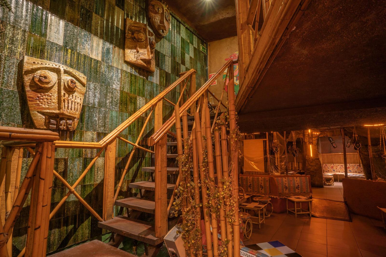 Escalera de bambú y máscaras tiki en pared de mosaico